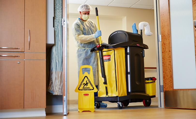 A team member in full PPE with a cleaning cart in a clinical room